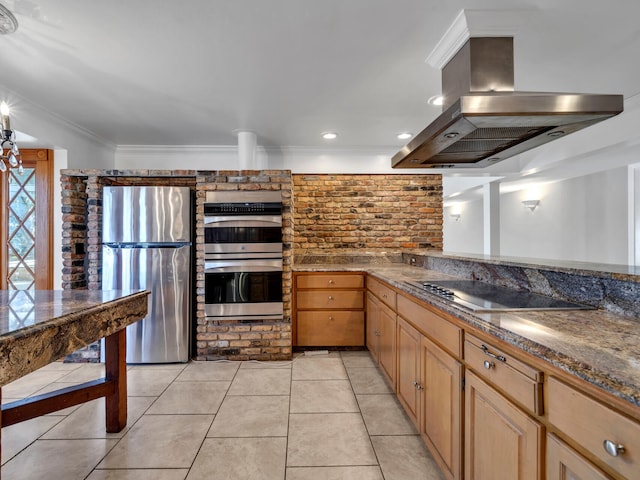 kitchen with ornamental molding, dark stone countertops, island exhaust hood, light tile patterned flooring, and stainless steel appliances