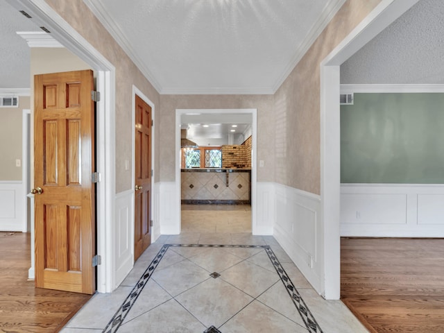 hall featuring a textured ceiling, ornamental molding, and wainscoting