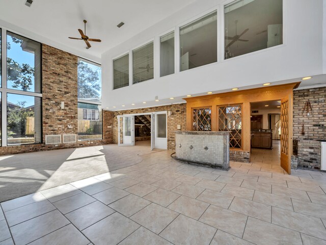 unfurnished living room featuring tile patterned floors, brick wall, and a ceiling fan
