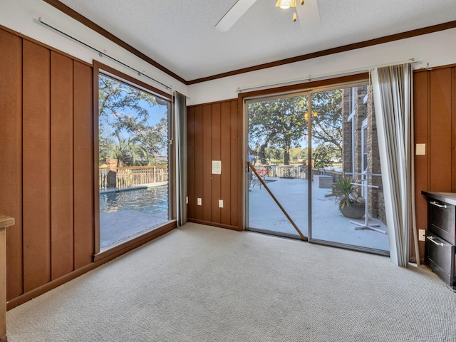 spare room with a textured ceiling, wooden walls, a ceiling fan, and light carpet