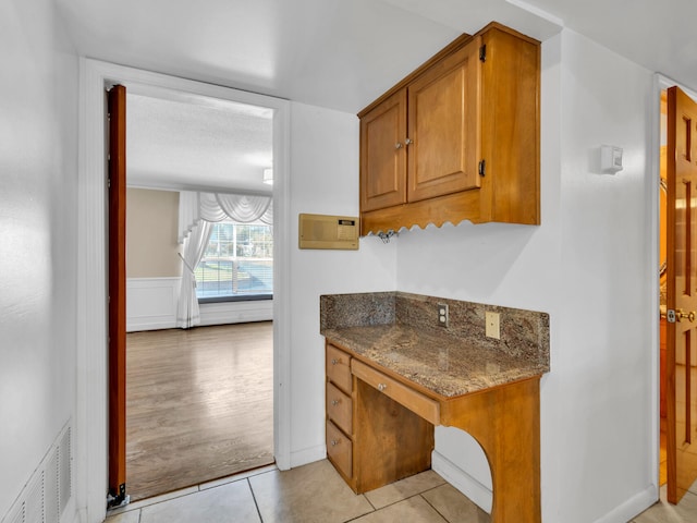 kitchen with visible vents, light tile patterned flooring, brown cabinetry, and dark stone counters