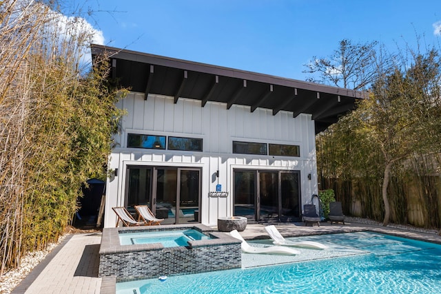 back of property with an outdoor pool, board and batten siding, and an in ground hot tub