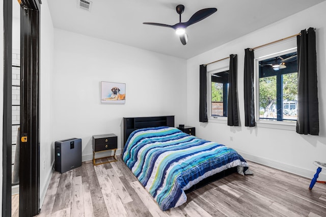 bedroom featuring a ceiling fan, visible vents, baseboards, and wood finished floors