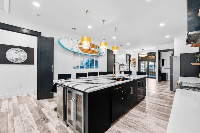 kitchen with a sink, light wood-type flooring, beverage cooler, and dark cabinets