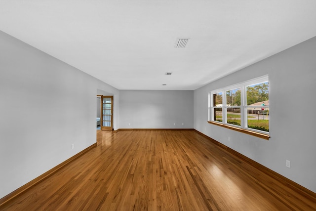 empty room featuring wood finished floors, visible vents, and baseboards