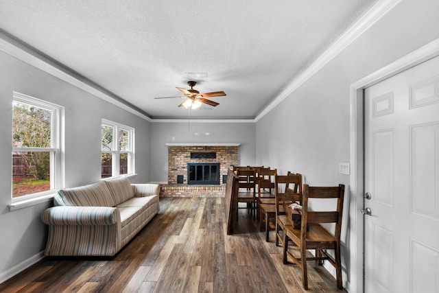 living area featuring a brick fireplace, crown molding, ceiling fan, a textured ceiling, and dark wood-style flooring