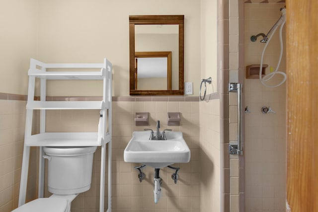 bathroom with a wainscoted wall, toilet, tile walls, and a stall shower