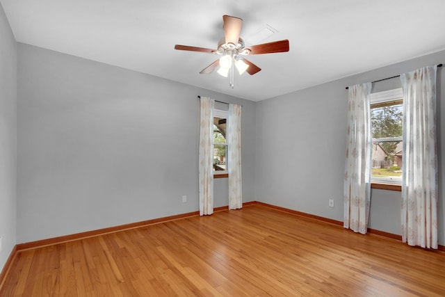 spare room featuring light wood finished floors, a ceiling fan, and baseboards