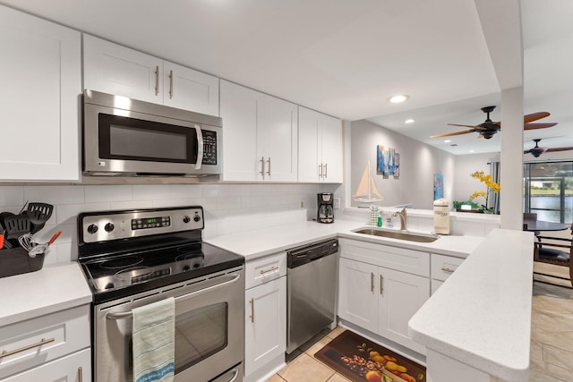 kitchen featuring stainless steel appliances, decorative backsplash, white cabinetry, a sink, and a peninsula