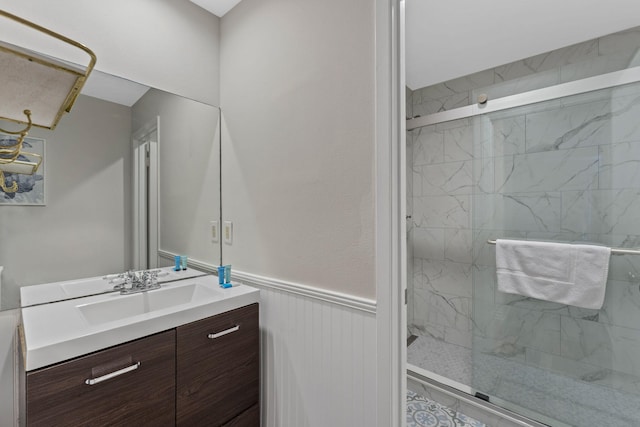 full bath with a wainscoted wall, a marble finish shower, and vanity