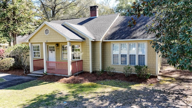 view of front of property with covered porch, roof with shingles, and a chimney