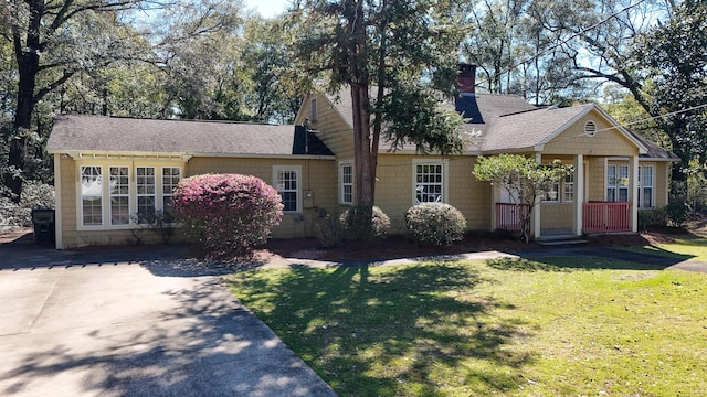 view of front of house with covered porch, a front lawn, a chimney, and a shingled roof