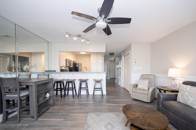 living area with ceiling fan, visible vents, dark wood-type flooring, and a wainscoted wall