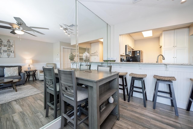 kitchen with stainless steel microwave, a kitchen breakfast bar, freestanding refrigerator, white cabinets, and a sink