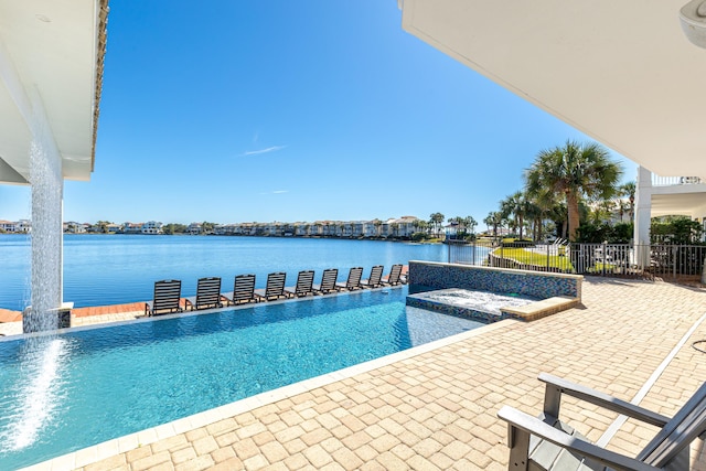 outdoor pool featuring a water view, a hot tub, fence, and a patio