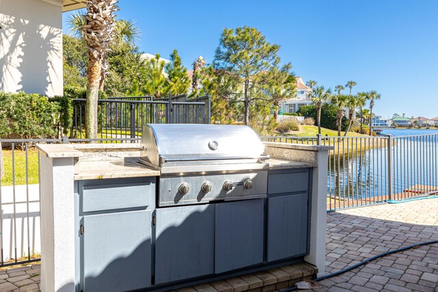 view of patio with exterior kitchen, a water view, a grill, and fence