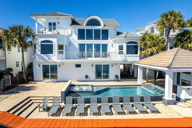 back of property with an infinity pool, a patio, fence, a balcony, and a tiled roof