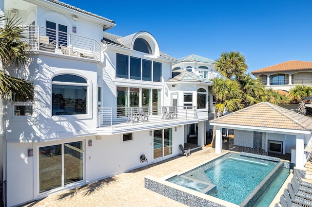 back of house with a balcony, a patio area, a tile roof, and stucco siding