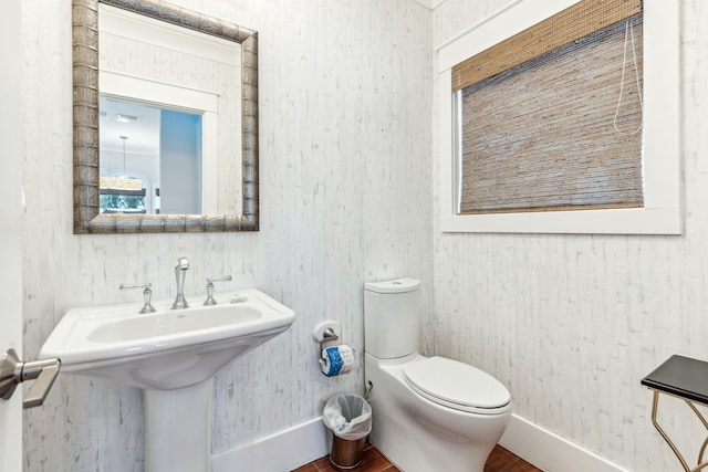 bathroom with wallpapered walls, a sink, toilet, and baseboards