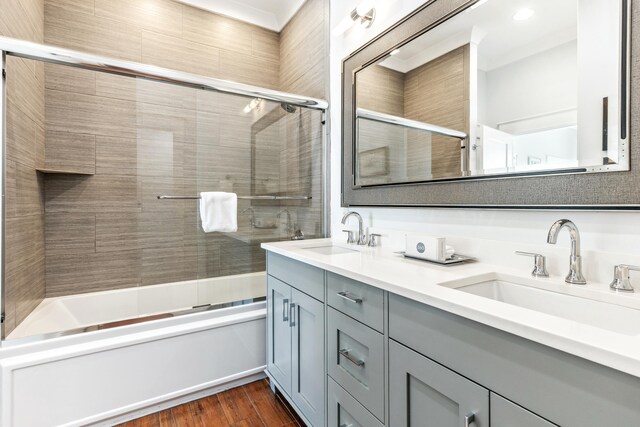 bathroom with double vanity, bath / shower combo with glass door, a sink, and wood finished floors