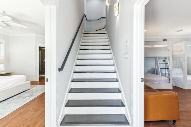 stairs with ceiling fan, baseboards, wood finished floors, and crown molding