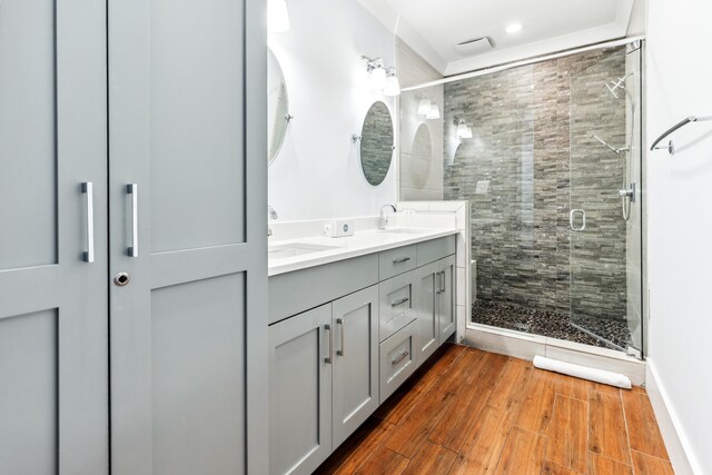 bathroom with double vanity, a stall shower, a sink, and wood finished floors