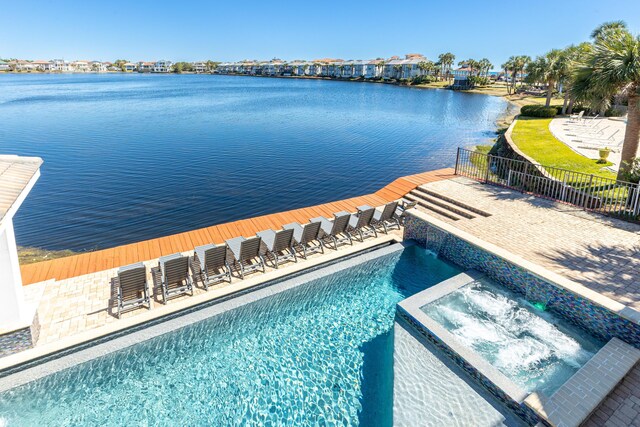 view of pool with a pool with connected hot tub, a water view, and fence