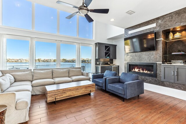 living area featuring visible vents, a water view, a premium fireplace, a ceiling fan, and wood finished floors