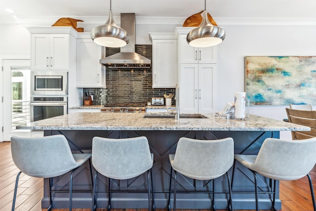 kitchen with wood finished floors, white cabinetry, appliances with stainless steel finishes, backsplash, and wall chimney exhaust hood