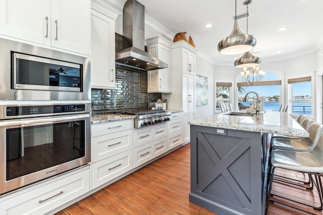 kitchen with appliances with stainless steel finishes, a sink, crown molding, wall chimney range hood, and backsplash