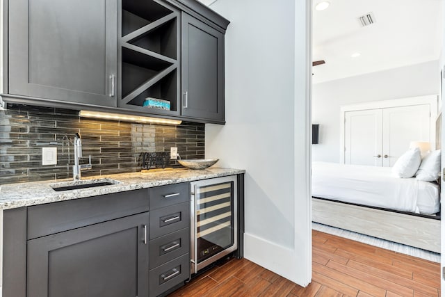 bar with beverage cooler, a sink, visible vents, decorative backsplash, and dark wood finished floors