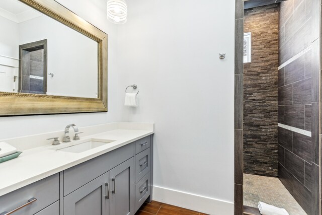 bathroom with wood finished floors, a tile shower, vanity, and baseboards