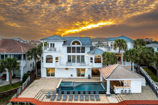 rear view of house with stucco siding, a pool with connected hot tub, a patio, a fenced backyard, and a balcony