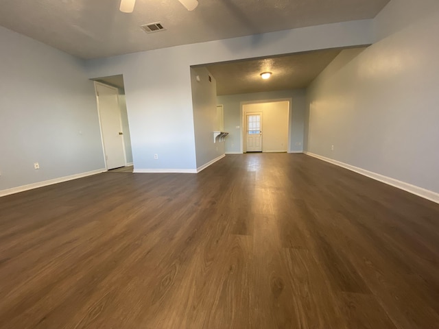 empty room with dark wood-type flooring, visible vents, ceiling fan, and baseboards