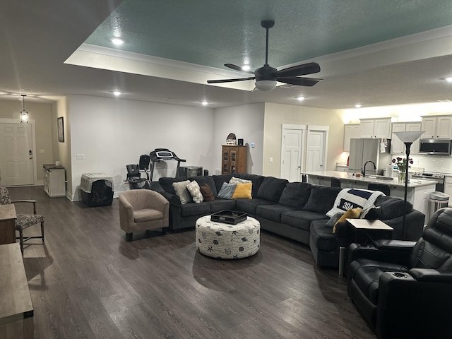 living area with a textured ceiling, a ceiling fan, baseboards, dark wood-style floors, and a tray ceiling