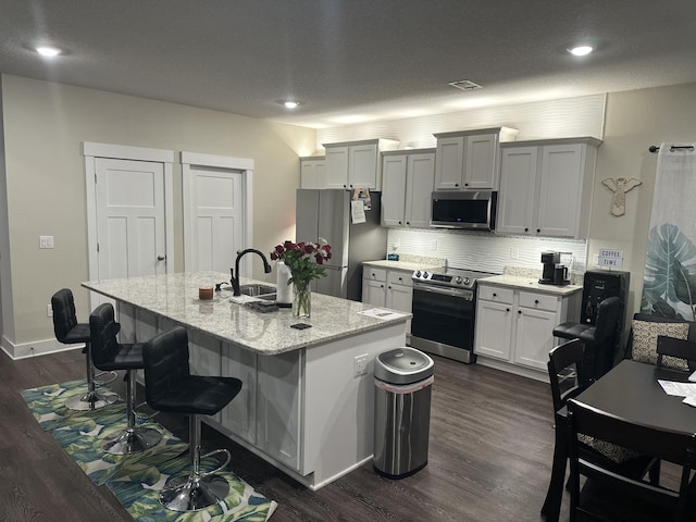 kitchen featuring a breakfast bar area, stainless steel appliances, white cabinets, an island with sink, and light stone countertops