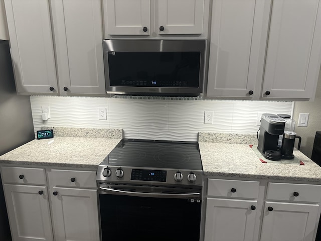 kitchen with appliances with stainless steel finishes, white cabinets, and backsplash
