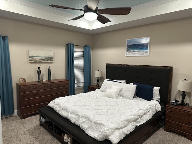 bedroom with light carpet, a tray ceiling, and a ceiling fan