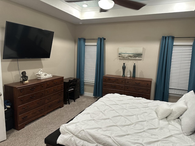 bedroom with light carpet, a tray ceiling, and a ceiling fan