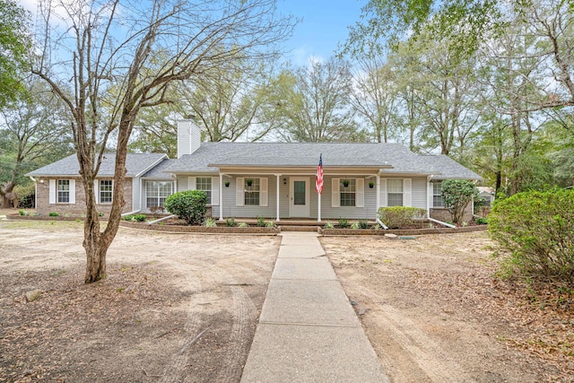 ranch-style home featuring covered porch, roof with shingles, and a chimney