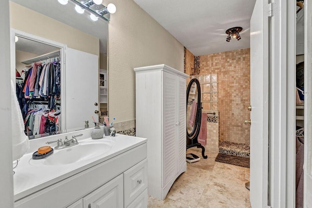 full bath featuring a walk in closet, a tile shower, vanity, and tile patterned floors