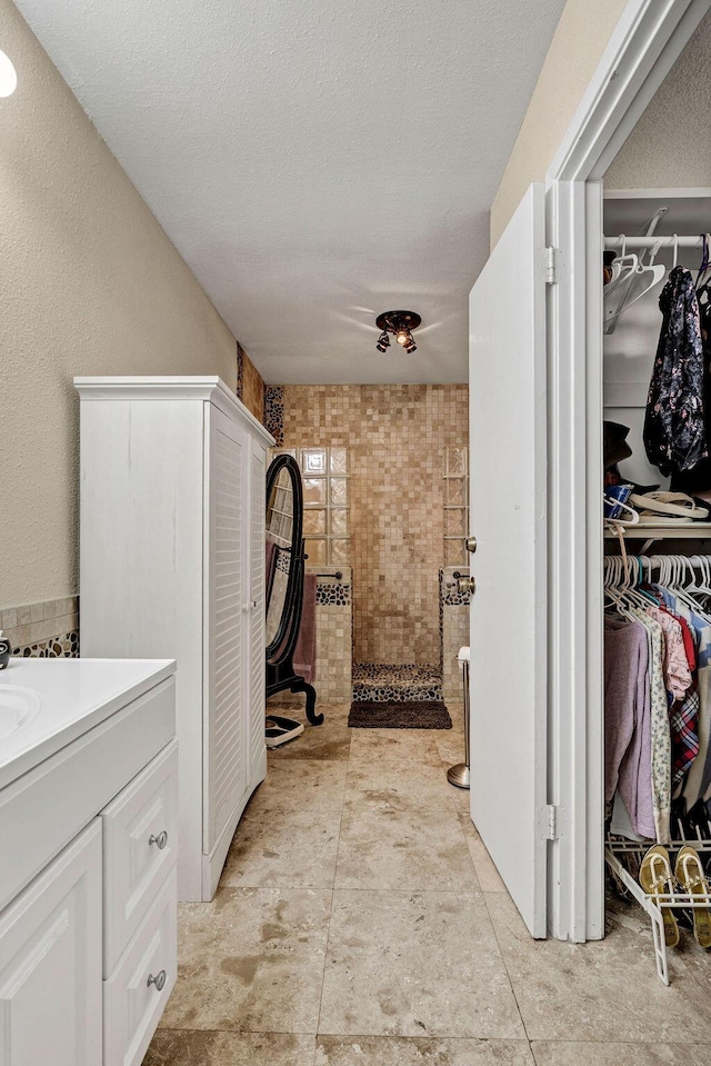 full bathroom with a spacious closet, vanity, a textured ceiling, and a walk in shower