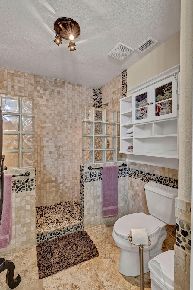 full bath with toilet, a textured ceiling, a walk in shower, and tile walls