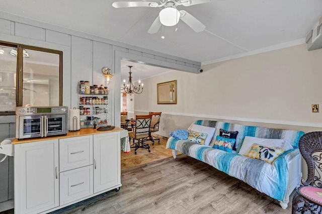 living room featuring ornamental molding, light wood-type flooring, and ceiling fan with notable chandelier