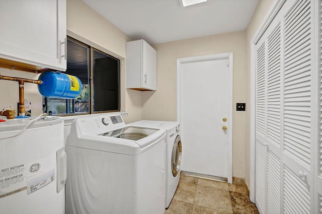 washroom featuring cabinet space, stone finish flooring, water heater, and independent washer and dryer