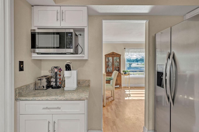 kitchen featuring light stone counters, light wood-style flooring, stainless steel appliances, baseboards, and white cabinets