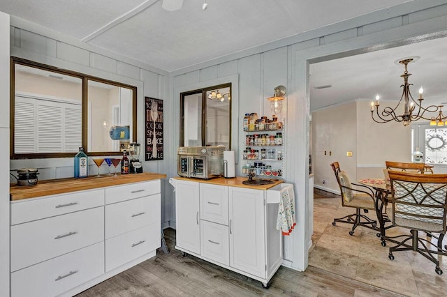 kitchen featuring a chandelier, hanging light fixtures, white cabinetry, butcher block countertops, and light wood-type flooring