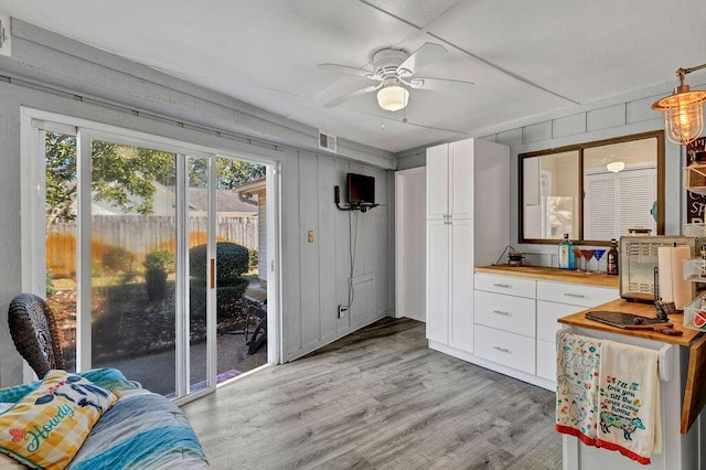 doorway to outside with a ceiling fan, light wood-type flooring, visible vents, and wooden walls