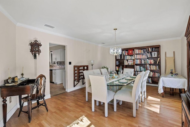 dining space with baseboards, visible vents, ornamental molding, light wood-style floors, and a notable chandelier