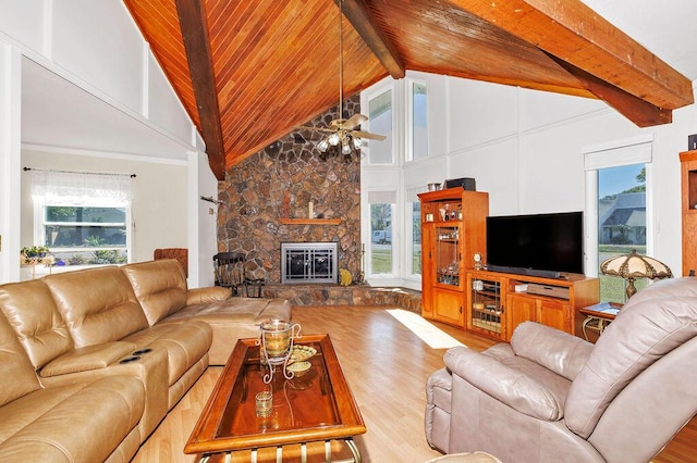 living area featuring a wealth of natural light, beam ceiling, a stone fireplace, and wood finished floors